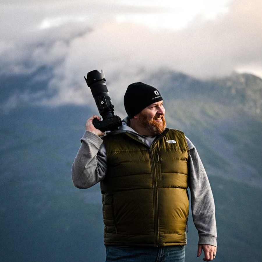 Jerrame holding his camera on a misty mountain summit