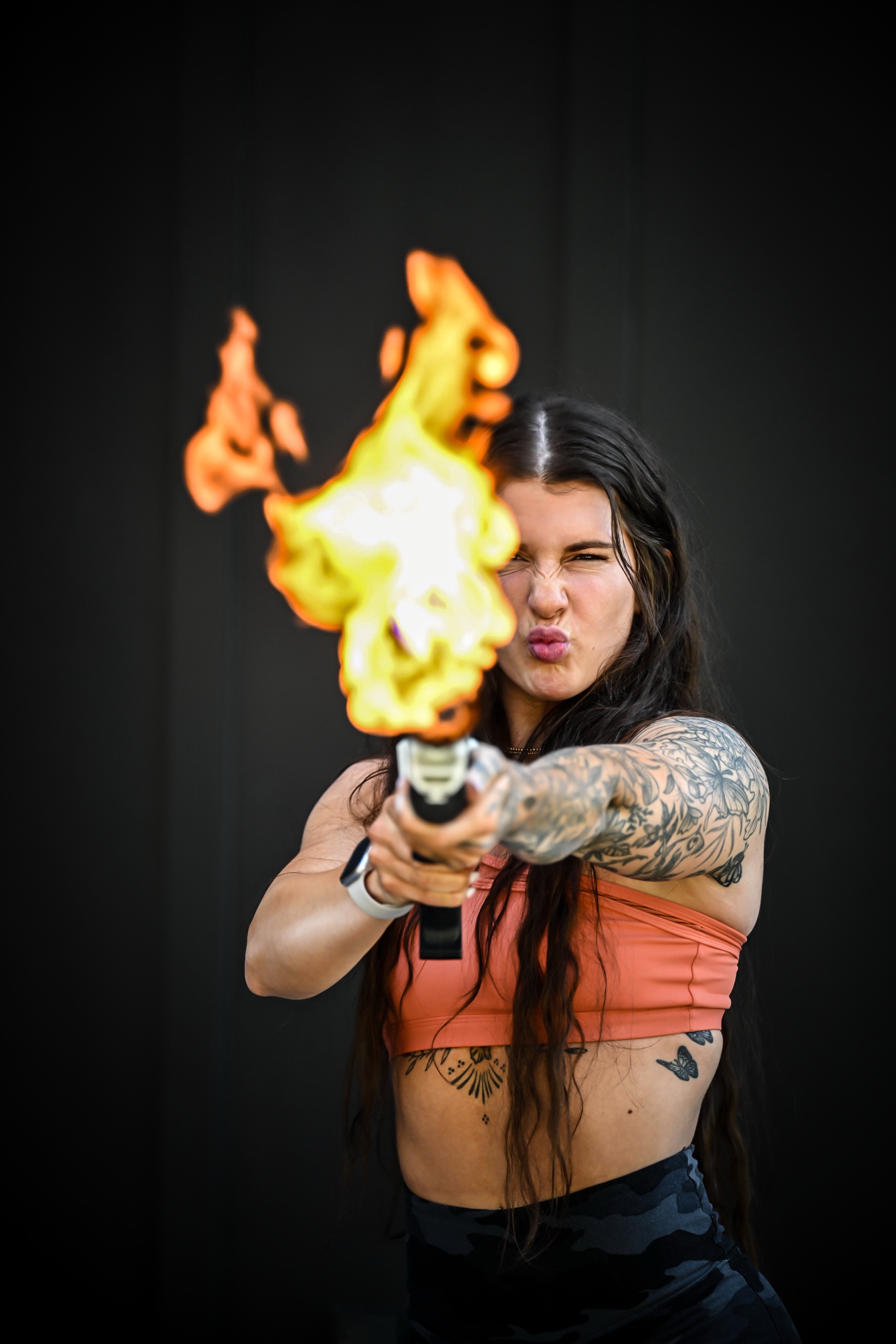 Woman with tattooed arms making a dramatic expression as a torch shoots a bright flame in front of her