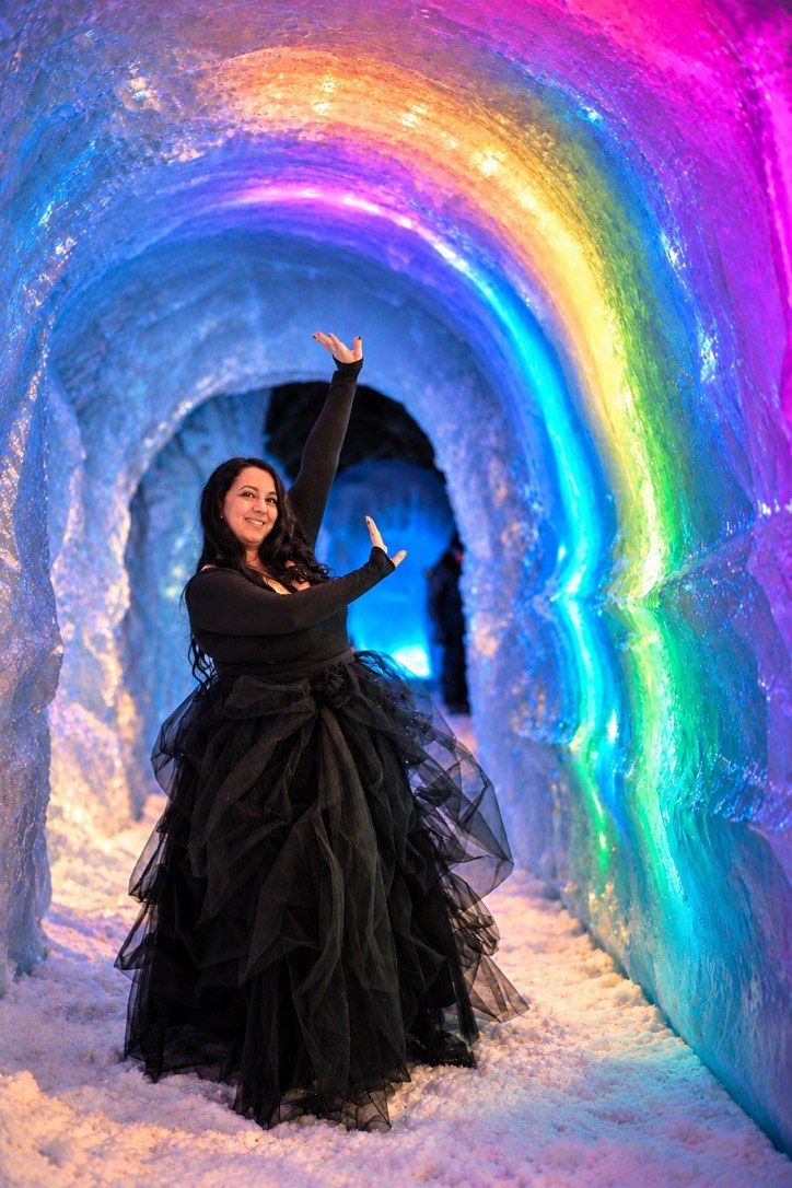 Woman in a black tulle gown posing inside a glowing, rainbow-lit ice tunnel