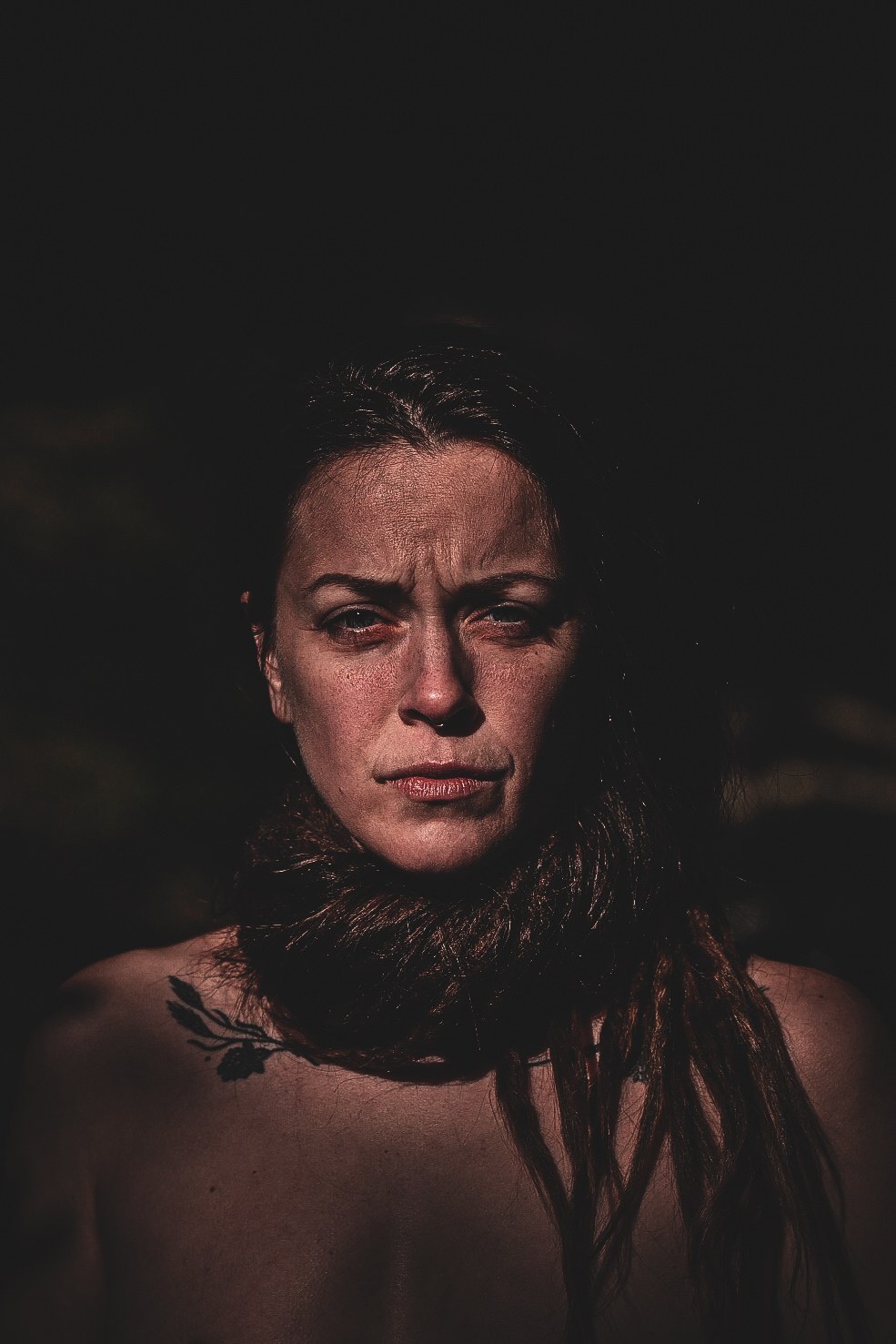 Moody close-up portrait of a woman lit by warm side light against a dark background