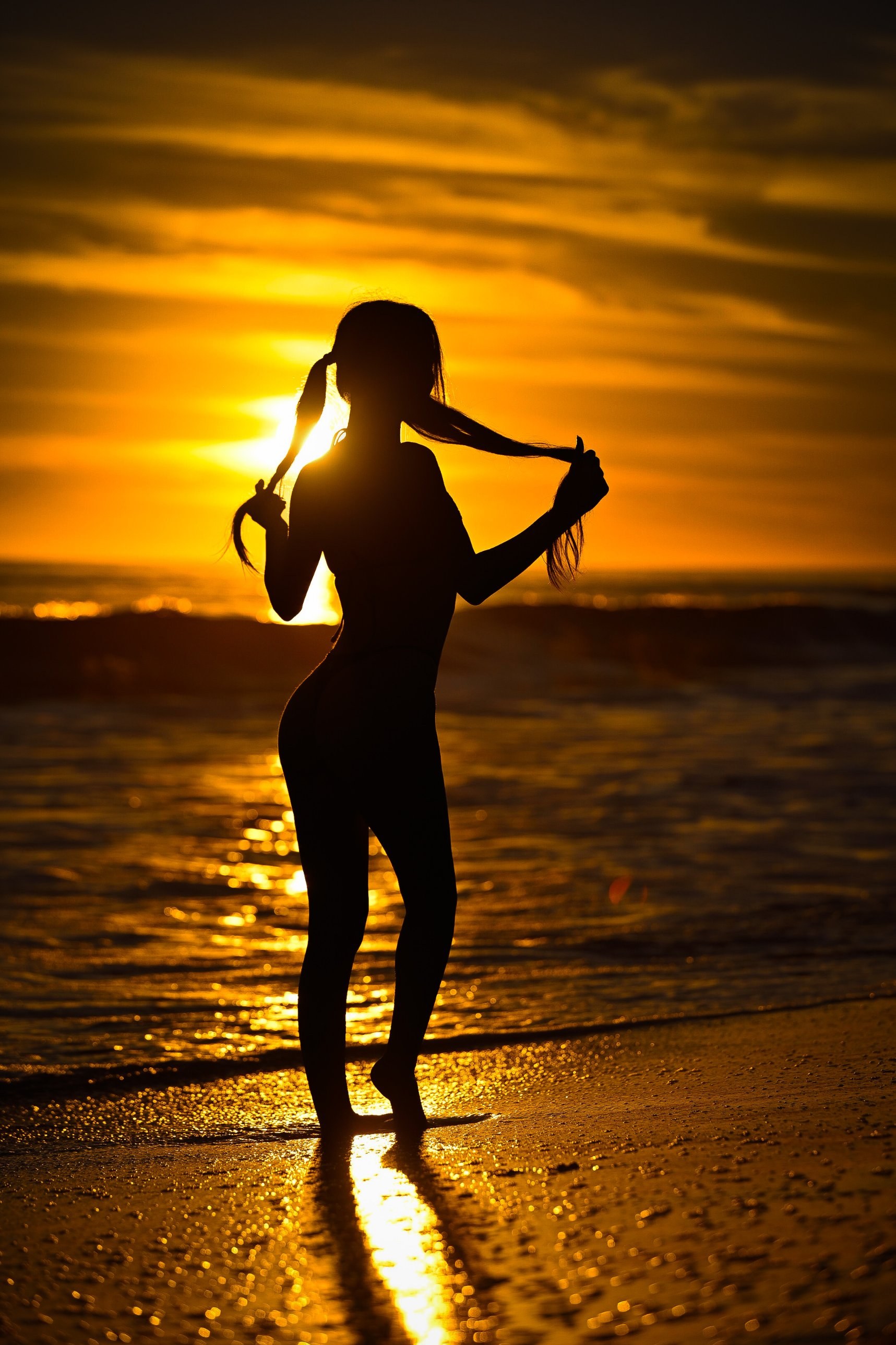 Silhouette of a woman in pigtails against a golden beach sunset