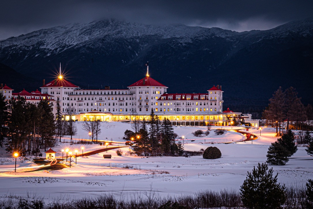 The Omni Mount Washington Hotel lit up at dusk, snow-covered mountains behind it