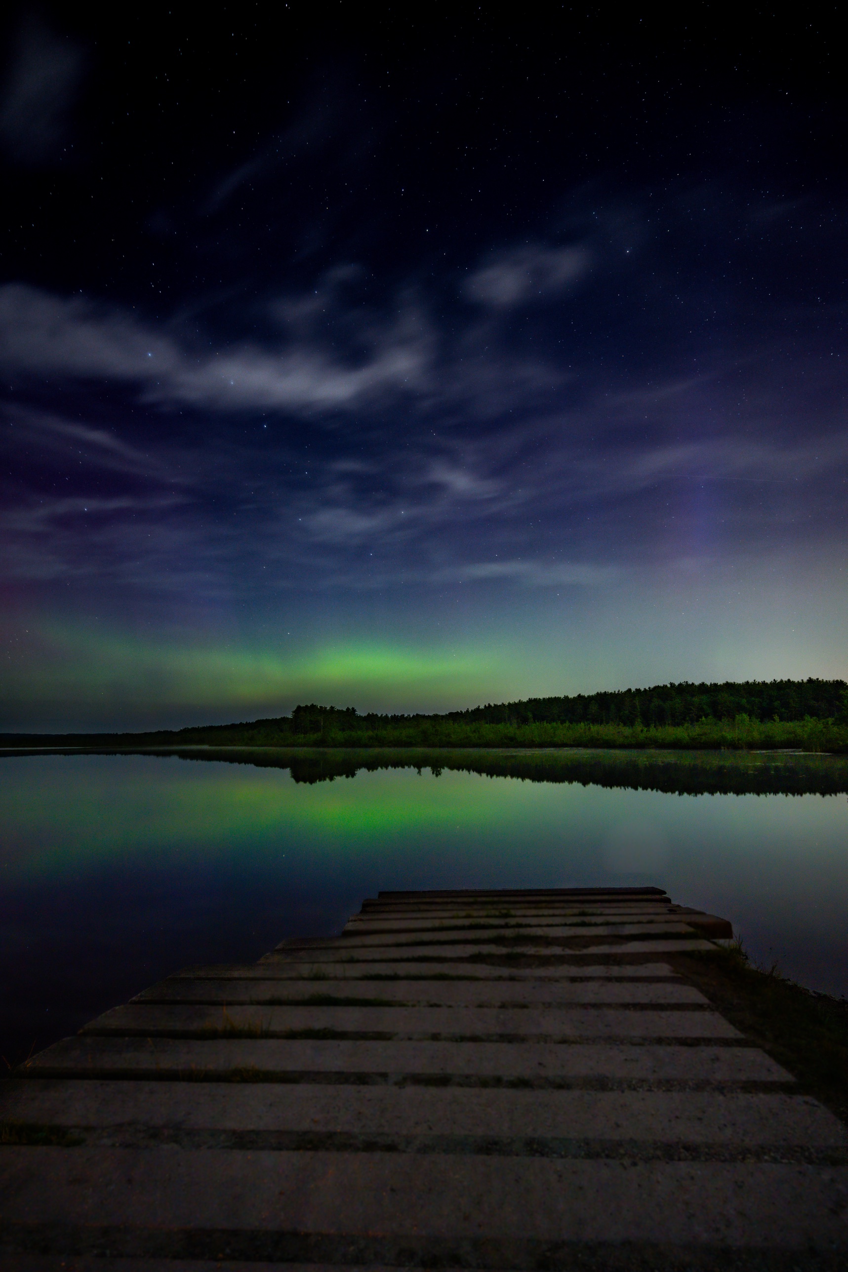 Aurora beams bending diagonally across the sky above a lake in Bow, New Hampshire