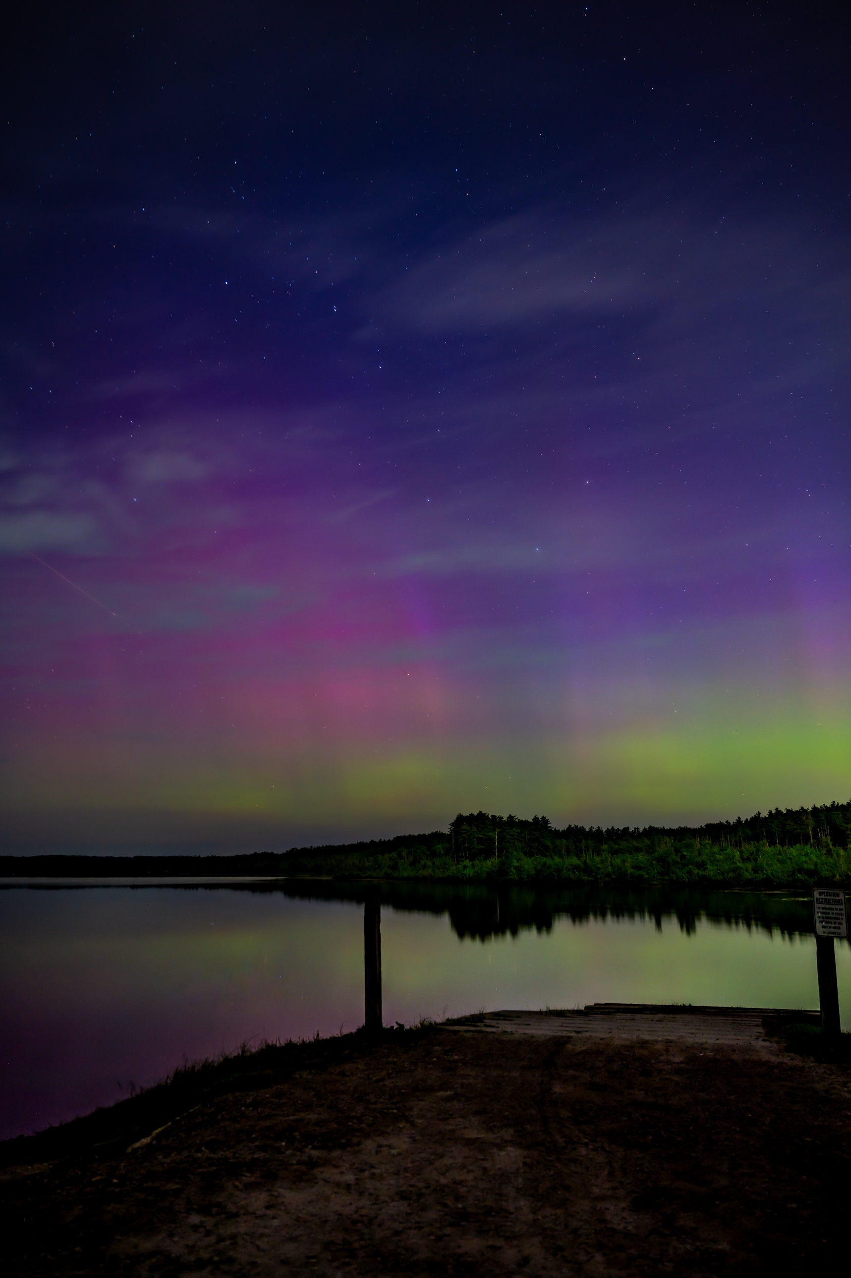 Aurora reflected on a still lake beyond a wooden dock in Bow, New Hampshire