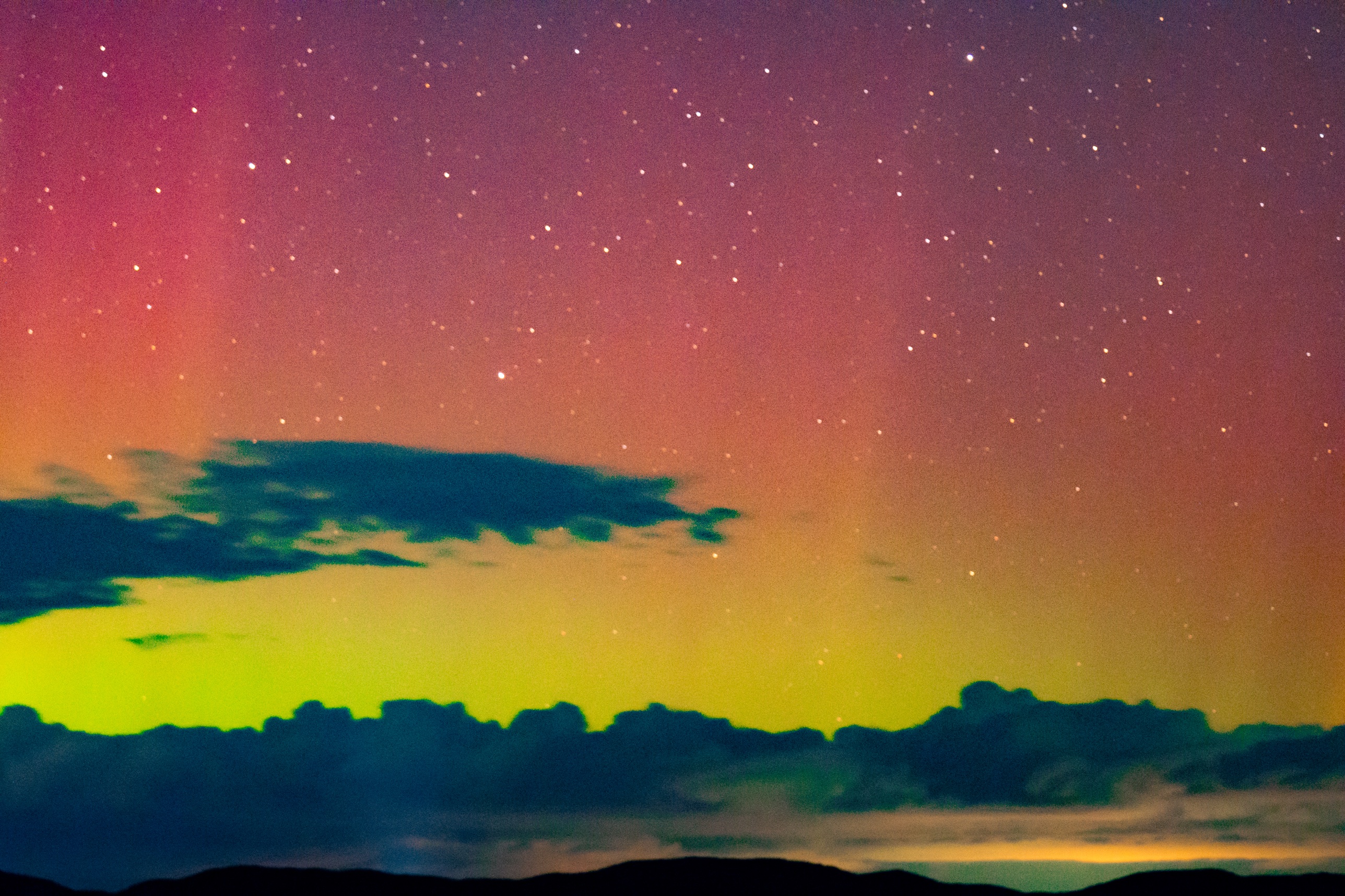 Pink, yellow, and green aurora glowing through a band of clouds over Gilford, New Hampshire