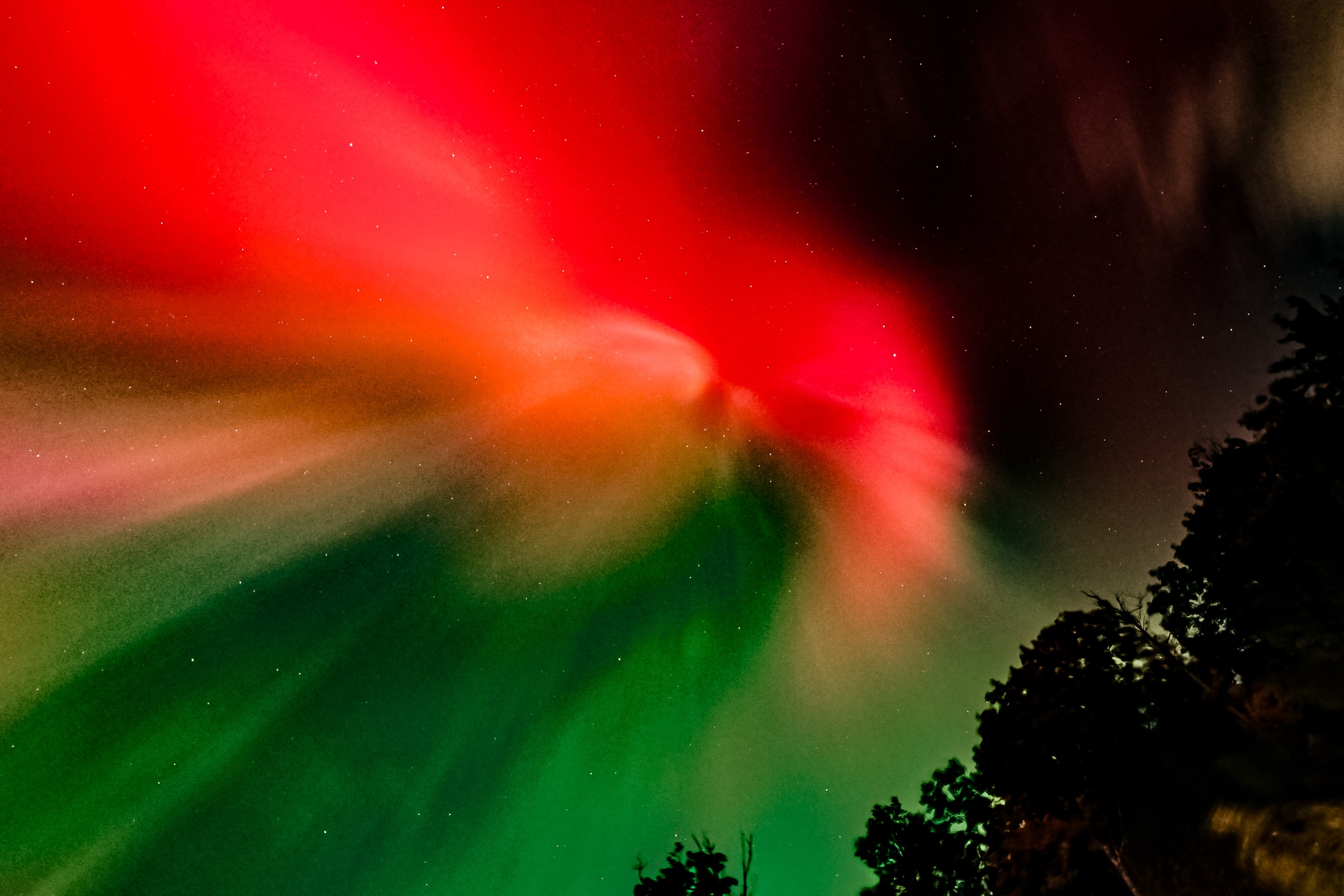 Close-up of red, orange, and green aurora light bending across the sky over Lake Winnisquam, New Hampshire