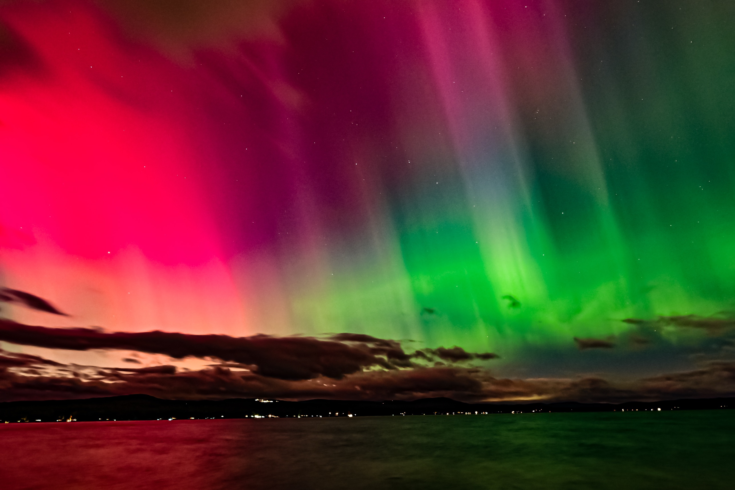 Aurora over Lake Winnisquam, New Hampshire, with the shoreline lit by distant town lights