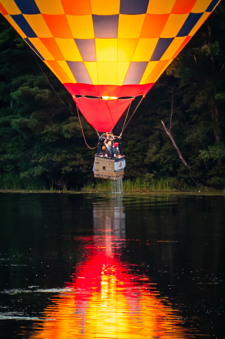 A hot air balloon firing its burner at the Suncook Rotary Hot Air Balloon Festival in Pittsfield, New Hampshire, the flame reflected on the lake