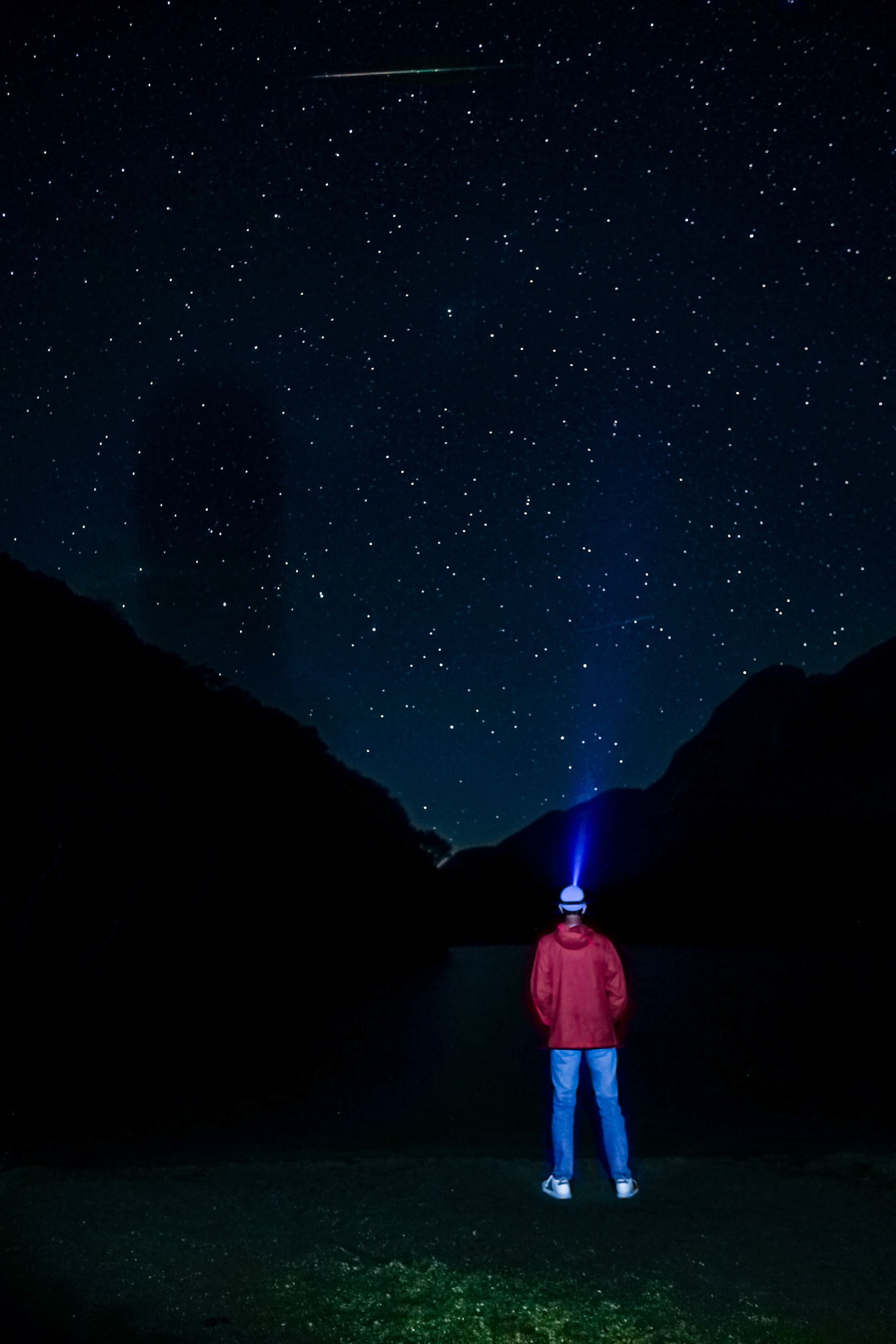 A stargazer's headlamp glowing beneath a meteor streaking over Profile Lake in Franconia Notch, New Hampshire