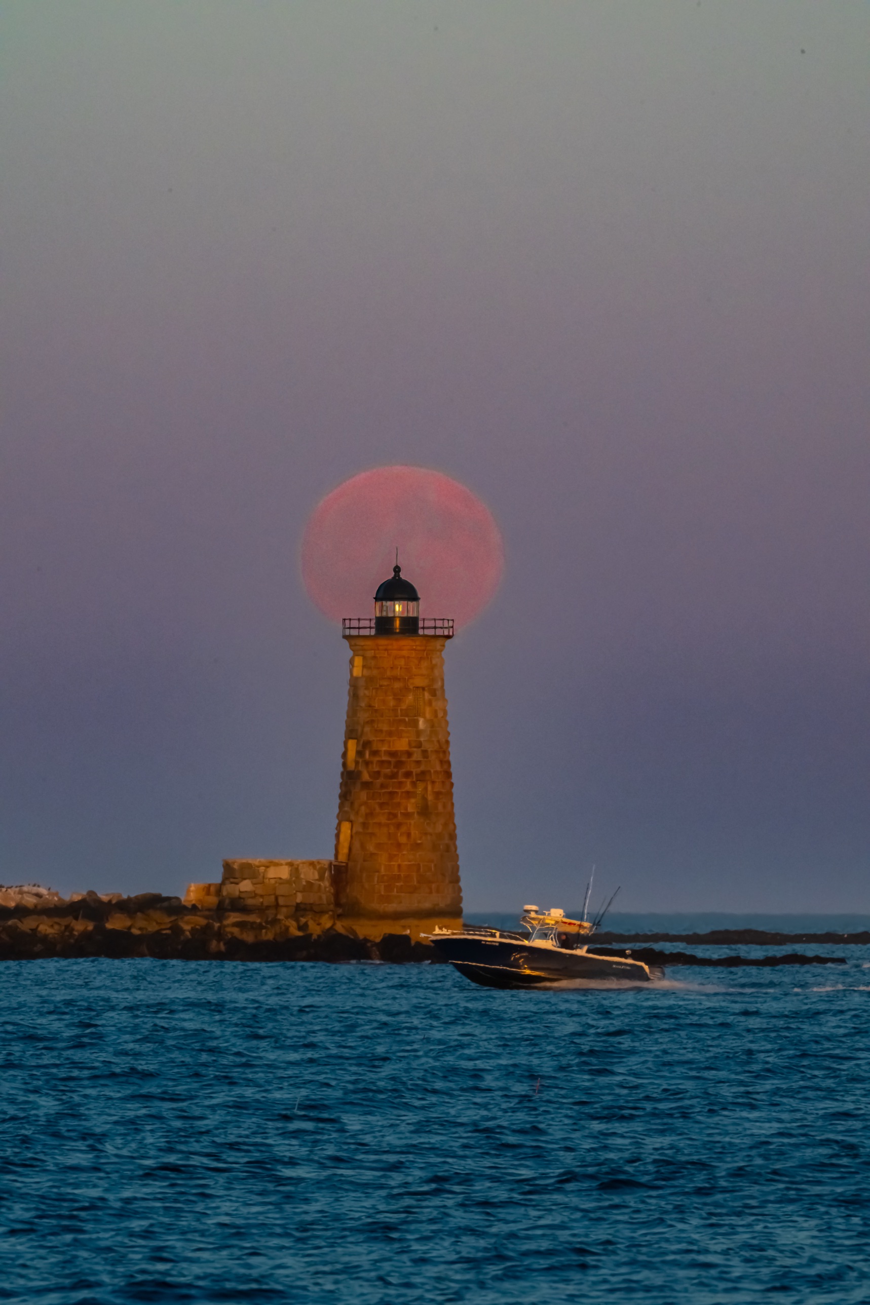Supermoon rising behind Whaleback Lighthouse in New Castle, New Hampshire, as a boat passes