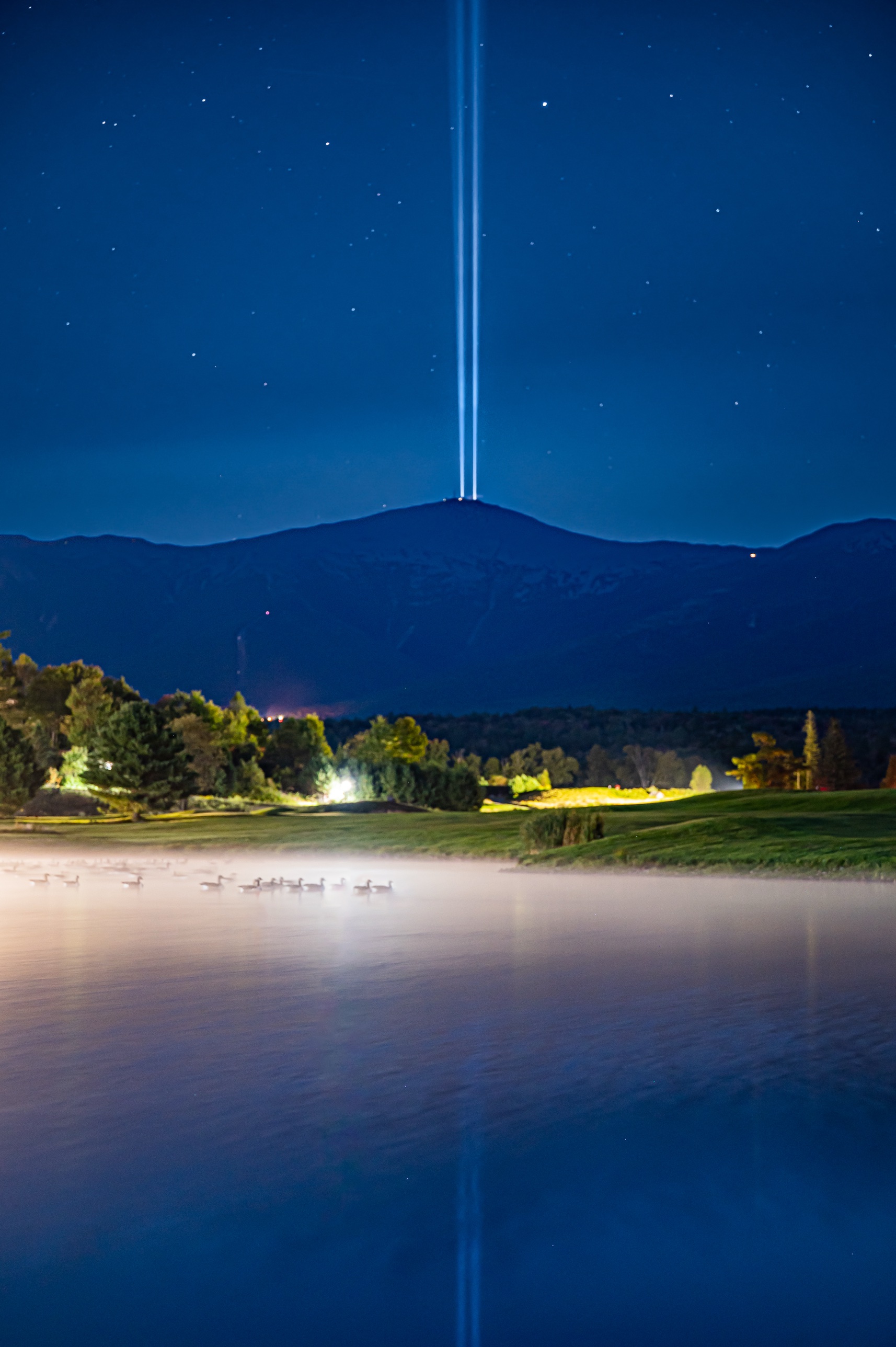 The 9/11 tribute light beams rising from the summit of Mount Washington over a foggy pond with geese