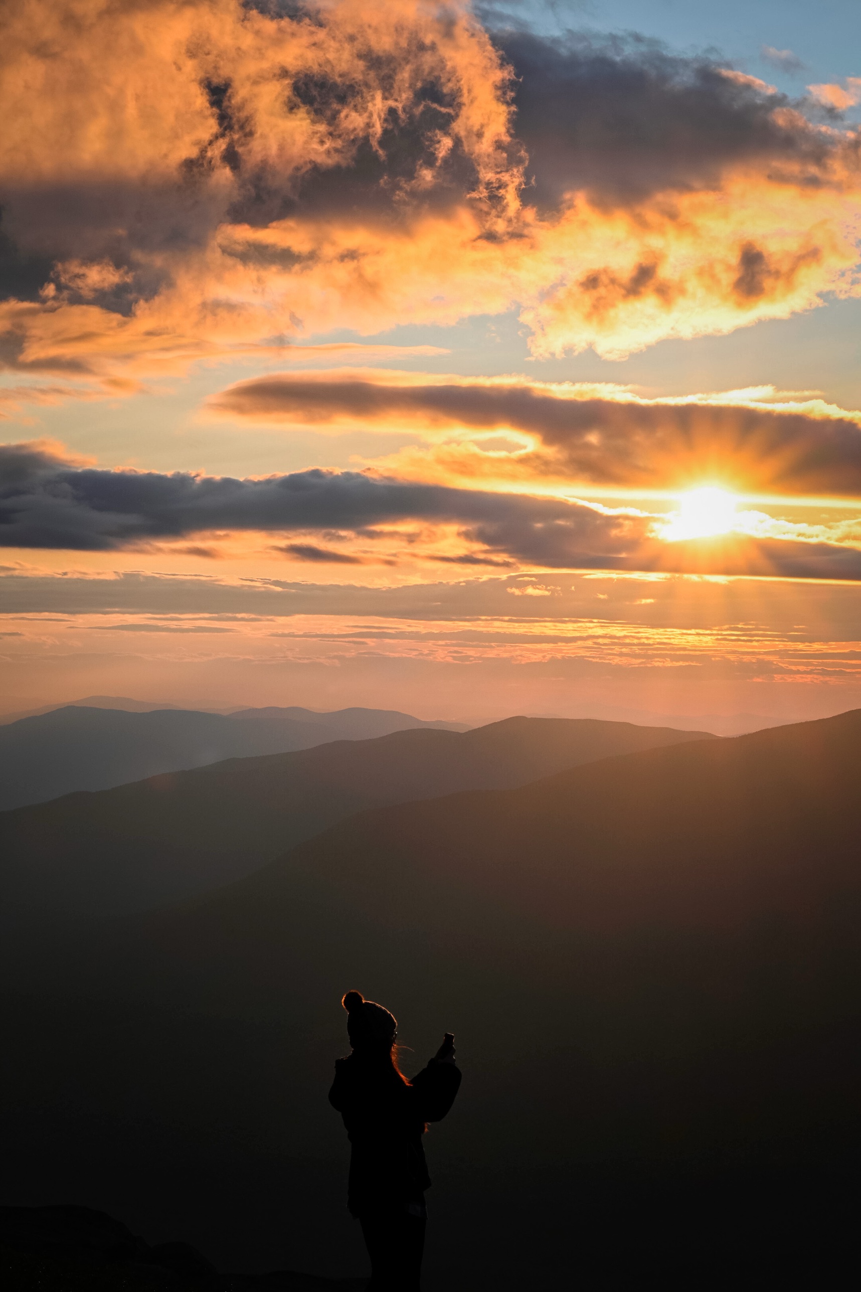 A hiker photographing the sunset from the summit of Mount Washington