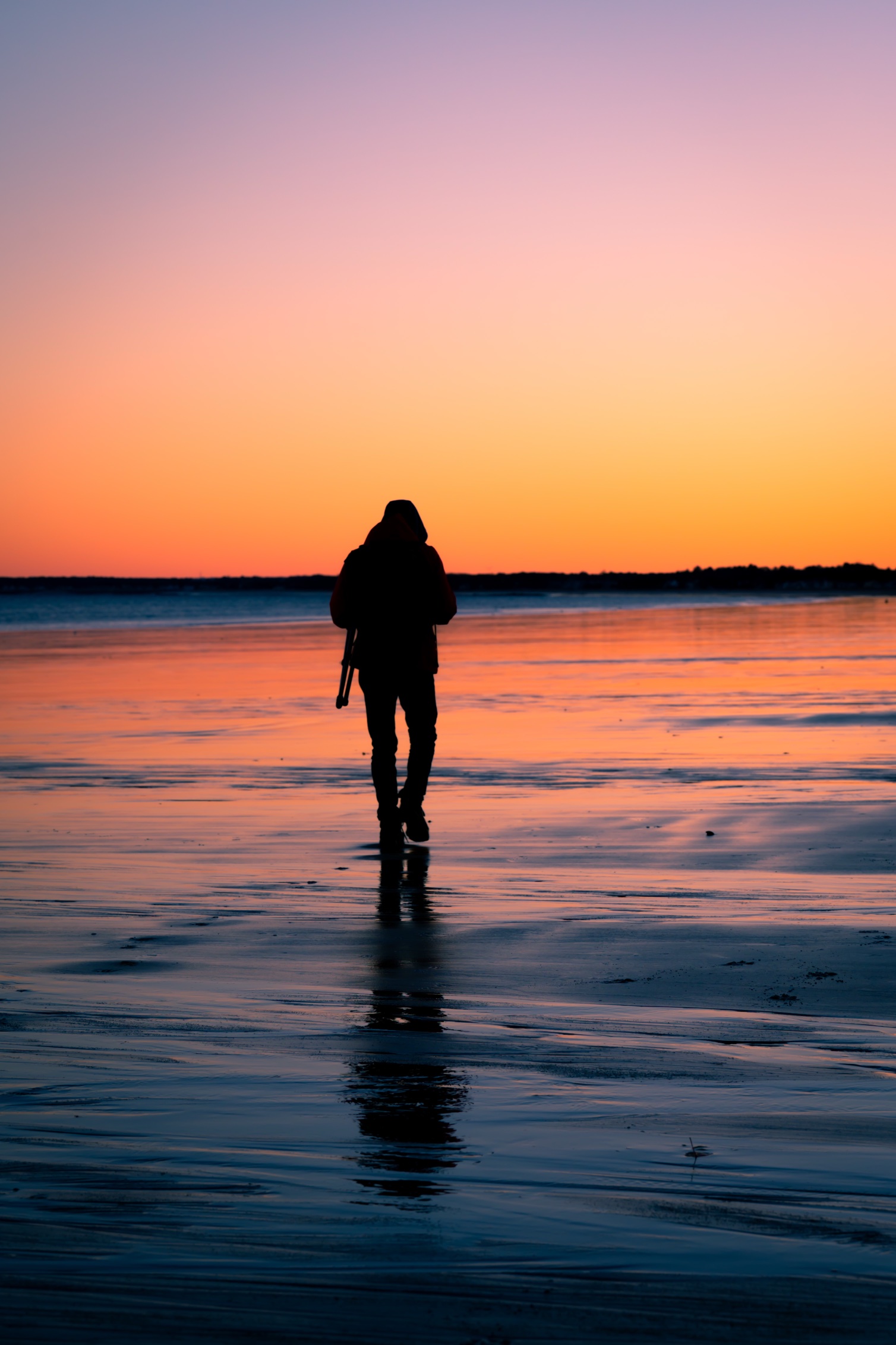 A photographer's silhouette walking the shore at sunset in Old Orchard Beach, Maine