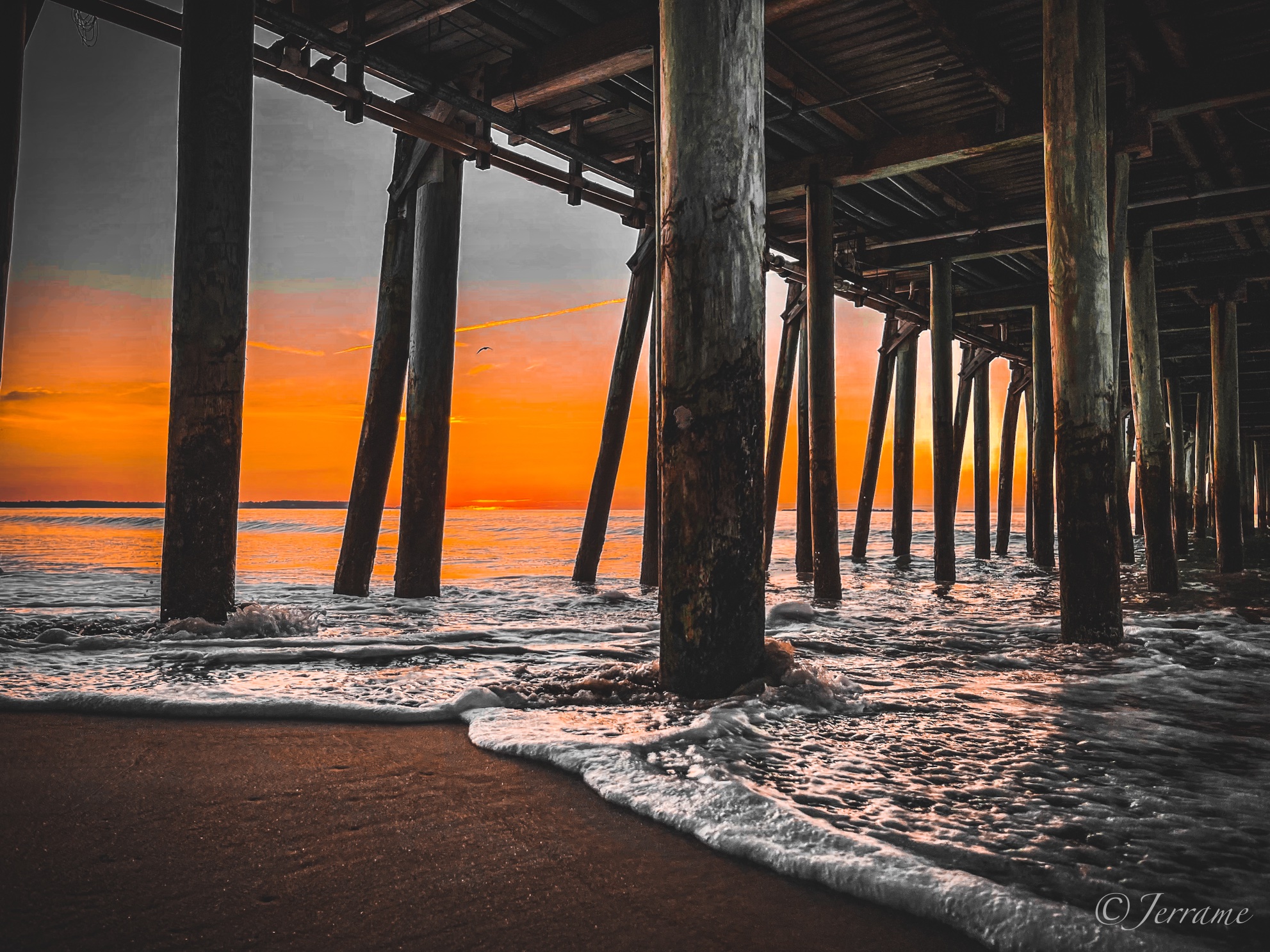 Sunrise glowing orange through the pilings beneath a weathered pier at Old Orchard Beach, Maine