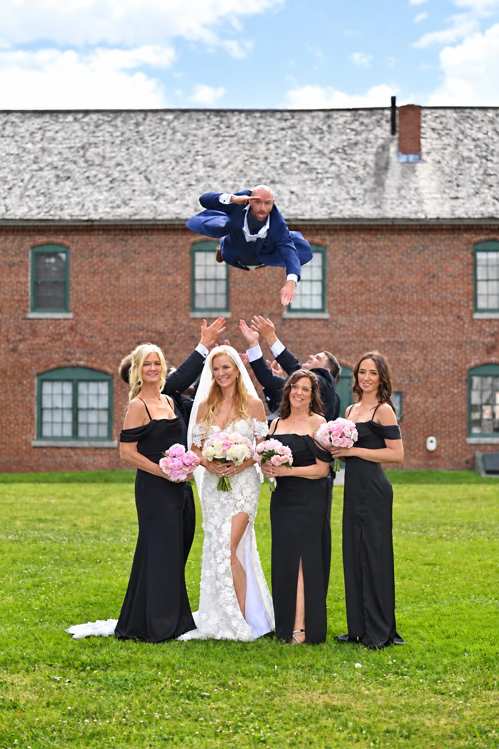 Bridesmaids and groomsmen tossing the groom into the air in front of a brick building