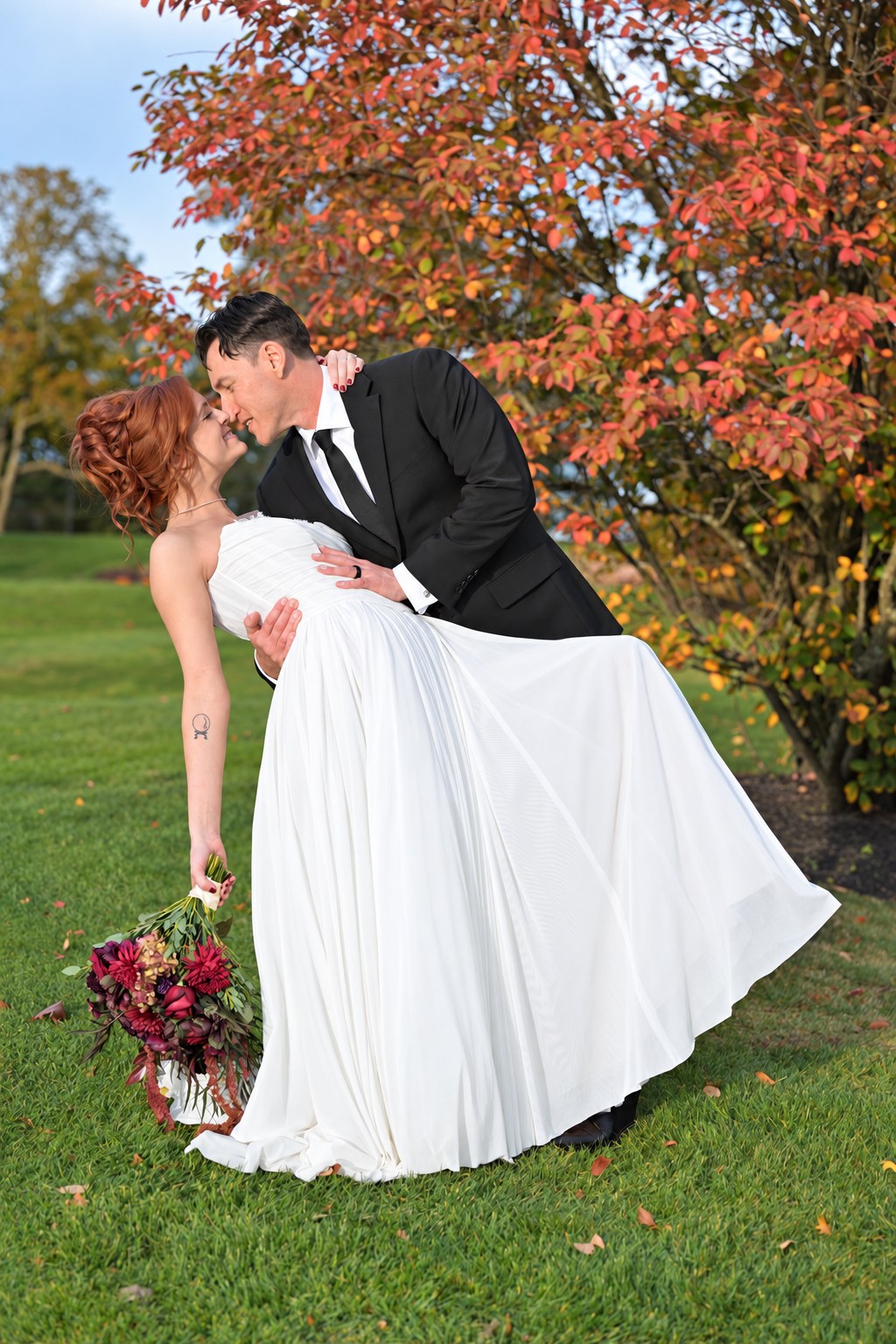 Groom dipping and kissing the bride beneath a tree in fall color